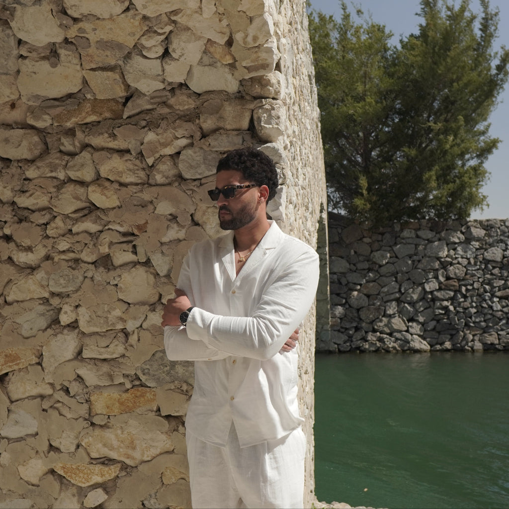 Sher Valor Alabaster Set – men's ivory linen shirt and trousers, side profile against Mediterranean stone wall