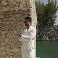Sher Valor Alabaster Set – men's ivory linen shirt and trousers, side profile against Mediterranean stone wall