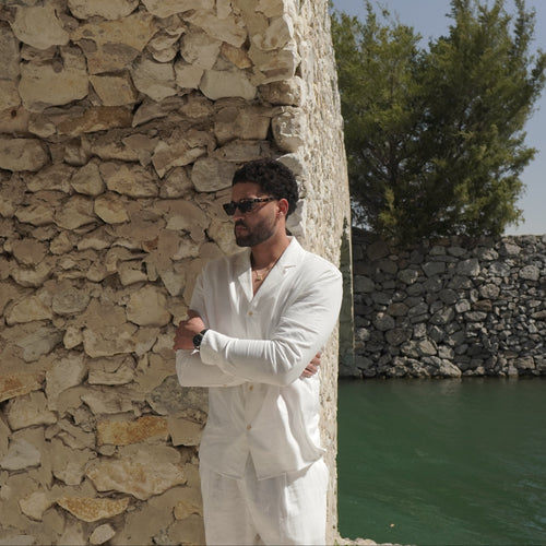 Sher Valor Alabaster Set – men's ivory linen shirt and trousers, side profile against Mediterranean stone wall